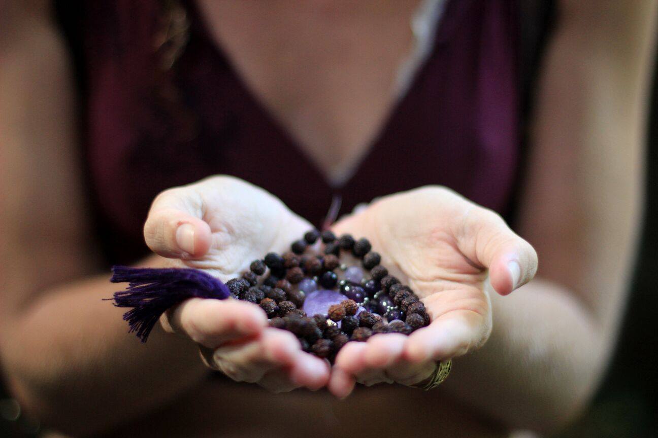 Cupped hands offering a mala of rudraksha beads and amethyst