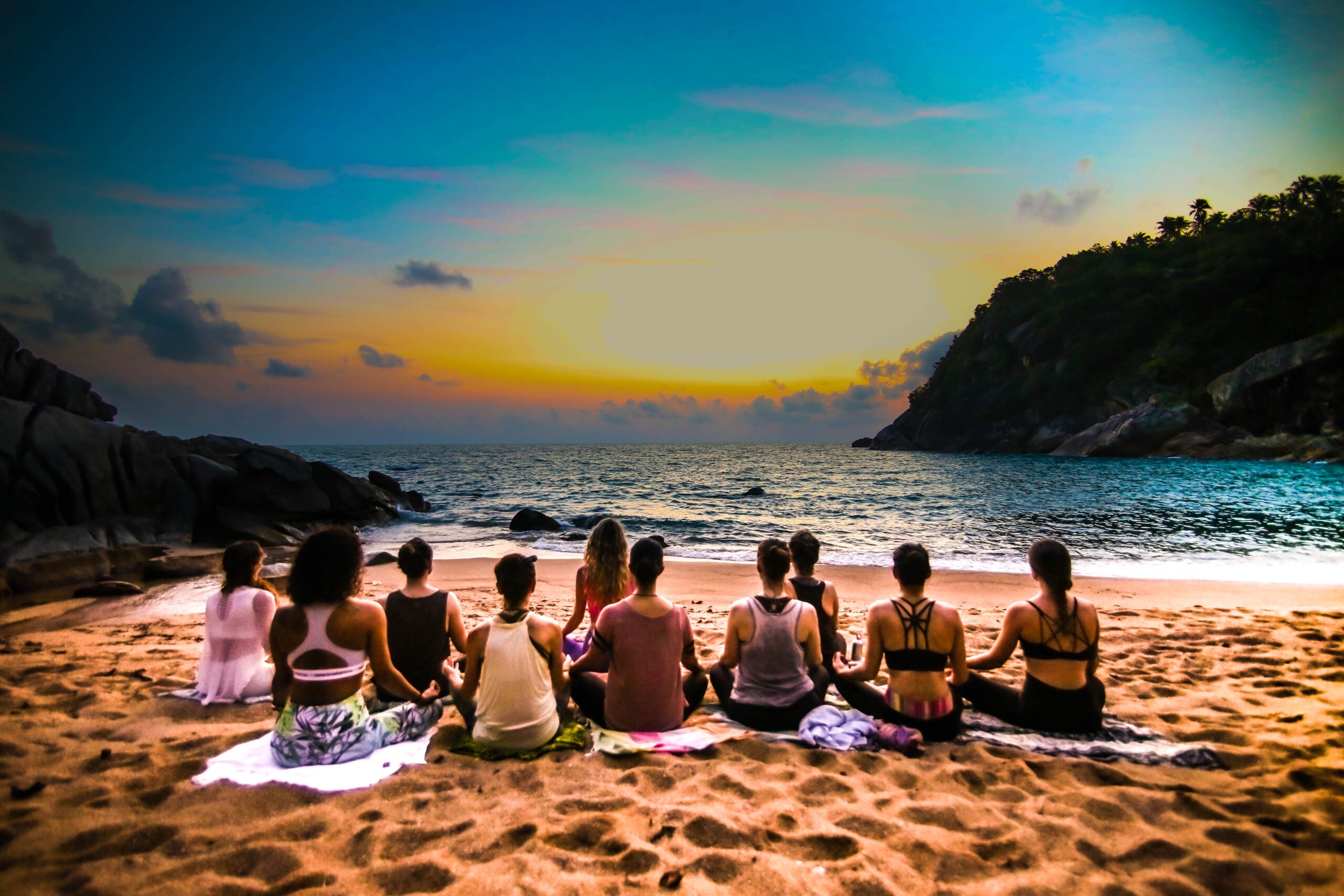 A group sitting in meditation on the beach at sunset on a Pure Flow Yoga retreat