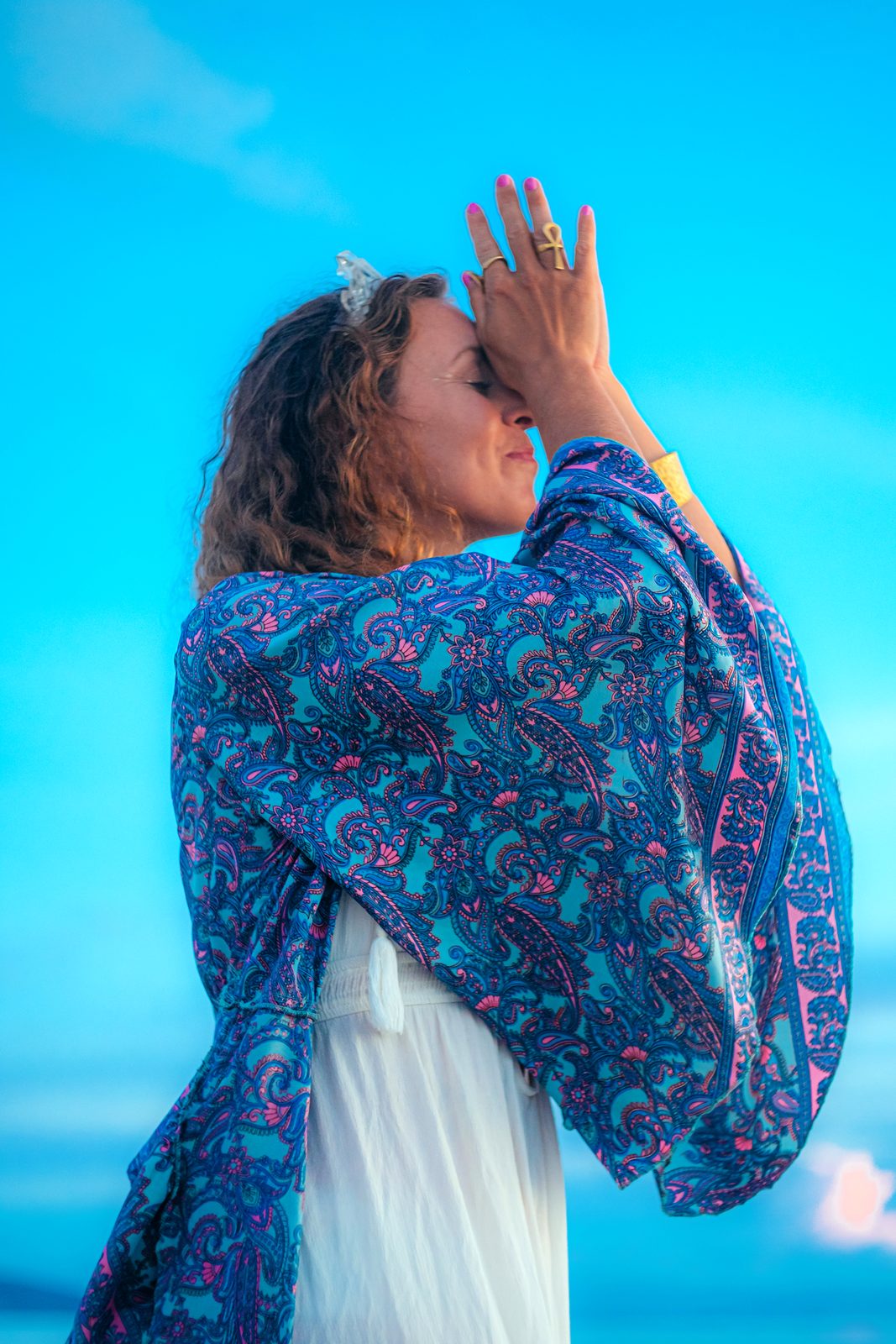 Francie in a blue paisley shawl, hand resting to her forehead in prayer against an open sky