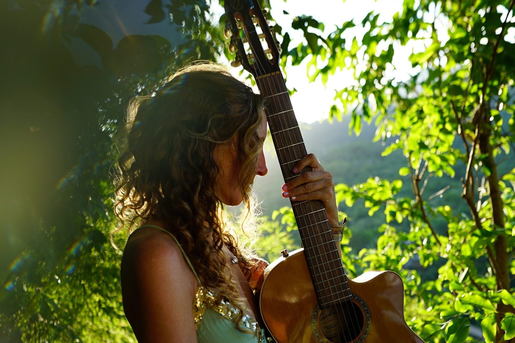 Francie La Flow resting her forehead against her guitar in the Bali jungle