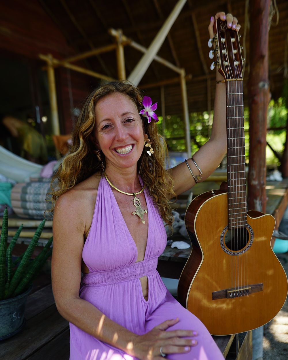 Francie La Flow smiling beside her guitar in a purple dress with a flower in her hair