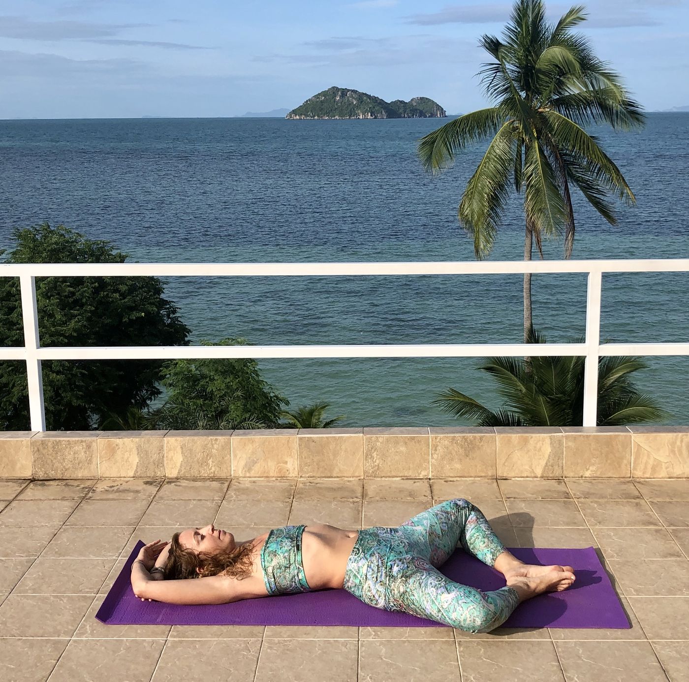 Francie in reclined bound angle pose on a purple mat by the sea